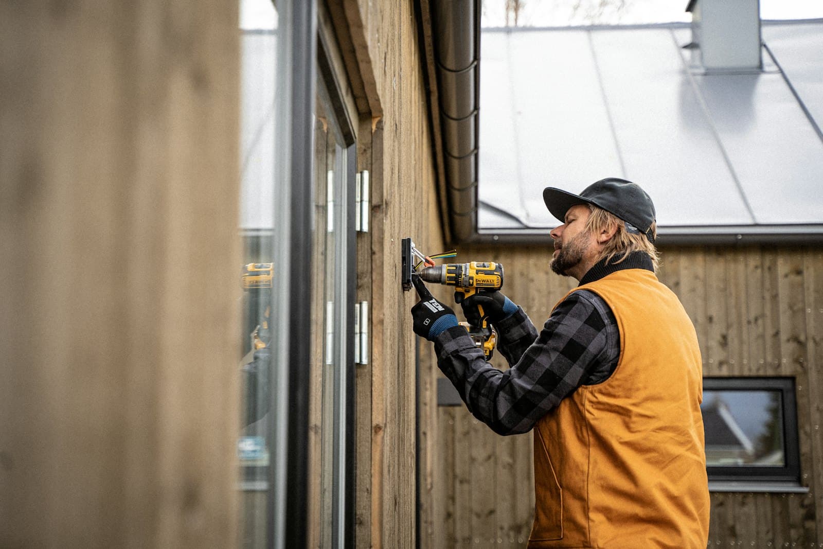 A tradesperson fitting an outdoor socket to timber cladding with a cordless drill.